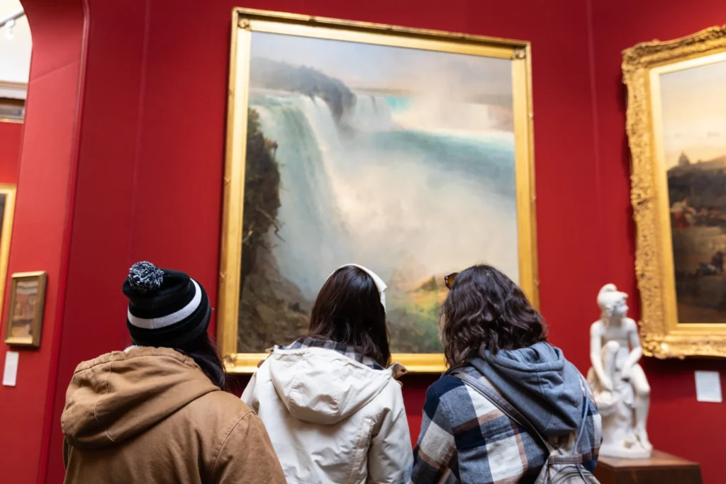 Three students look upward at an art piece in a museum.