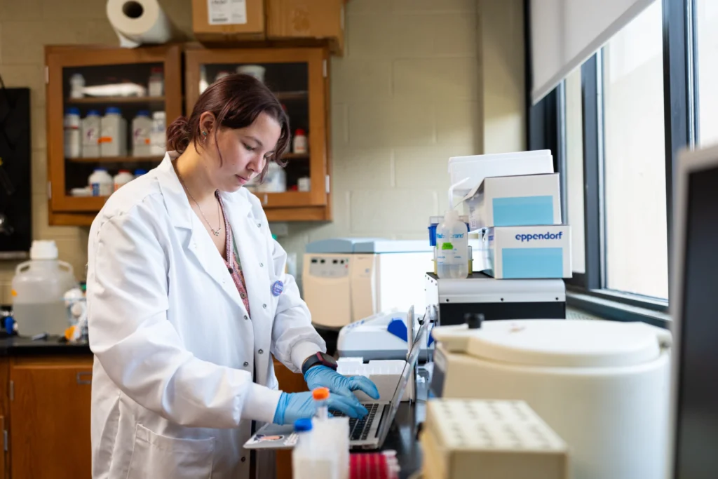 A biology student works on a laptop in a lab.