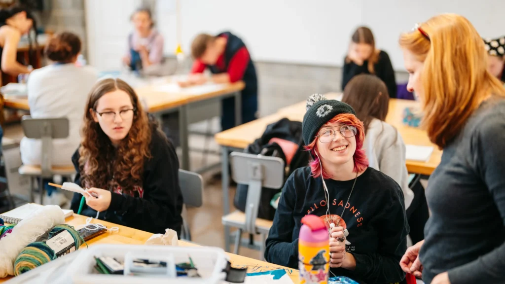 Art students work on their projects in class. One student speaks with their professor.