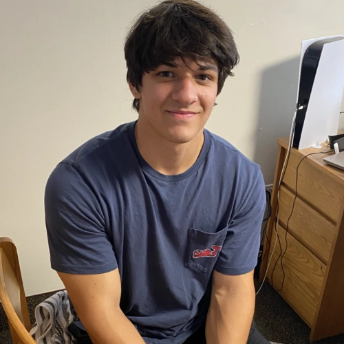 a student wearing a blue t-shirt sits in a dorm chair and smiles