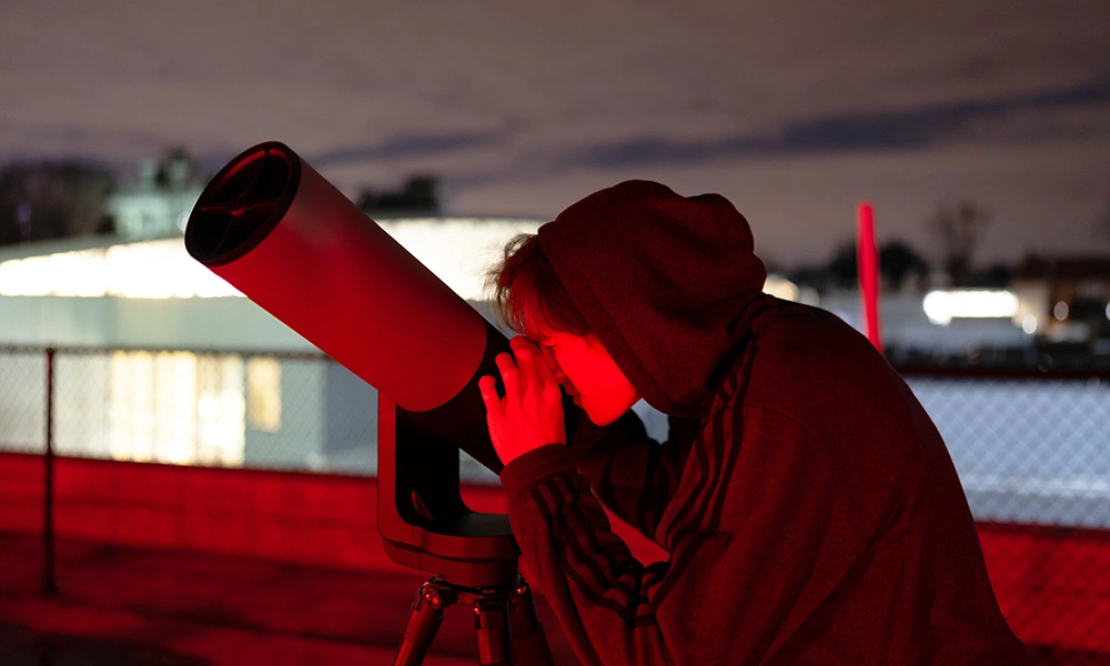 A student works outdoors with a telescope on the roof top Observatory at Boyer Hall of Science.