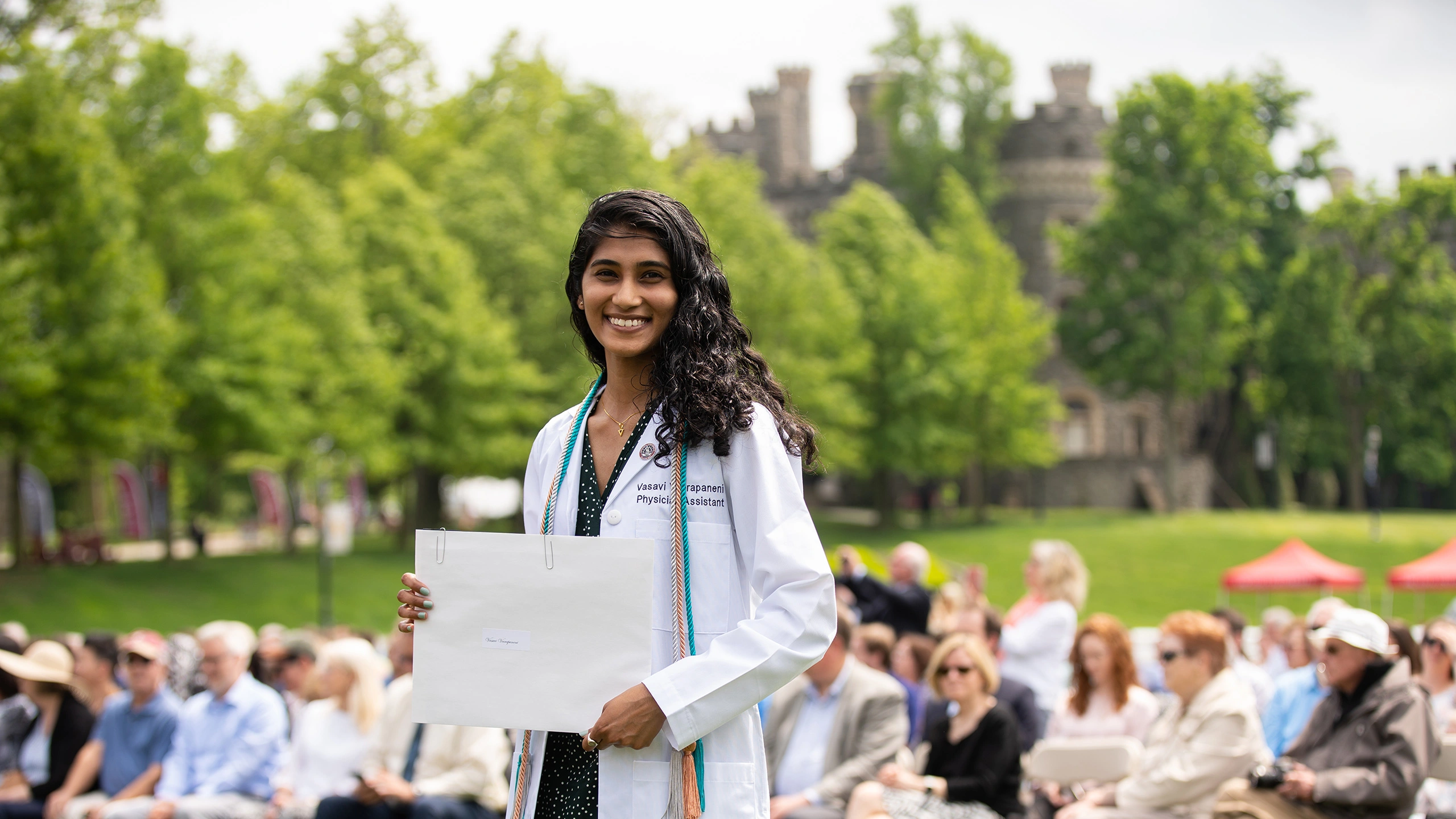A PA student holds her diploma and smiles during the white coat commencement ceremony.