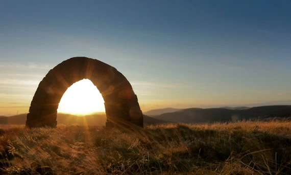 Arched rock formation with sunset on pretty Scottish field