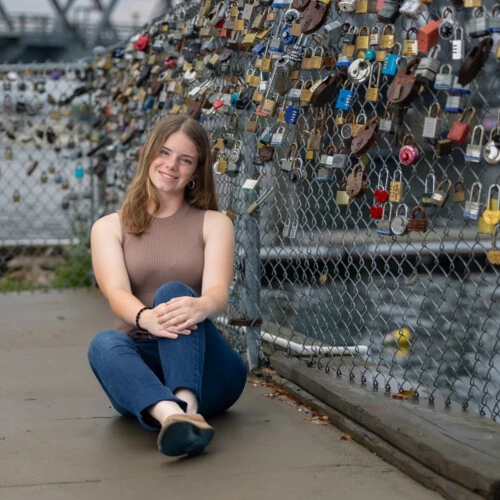 Ella Walsh sitting on the ground next to a fence with padlocks attached to it.