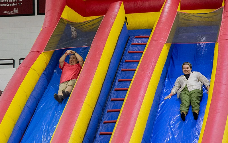 Two women sliding down an inflatable slide.