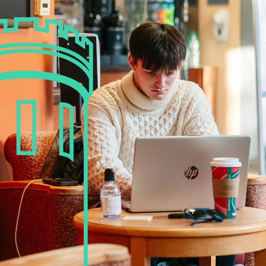 A student wearing a cable knit sweater works on an HP laptop in a student louge area on campus.