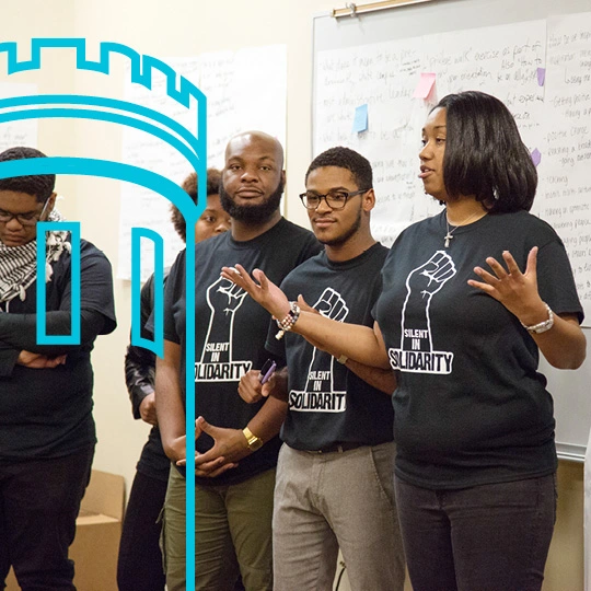 Five people stand during a meeting in front of a white board and all are wearing Silent in Solidarity t-shirts.