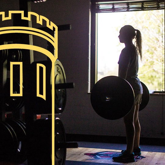 A student lifts weights in a darkly lit gym.