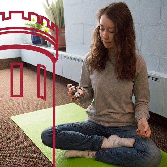 A student sits in a yoga pose and hjolds two silver balls in her hand.