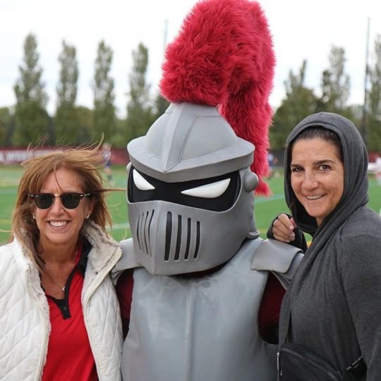 Two Arcadia alumni stand by Archie on a green field on campus.