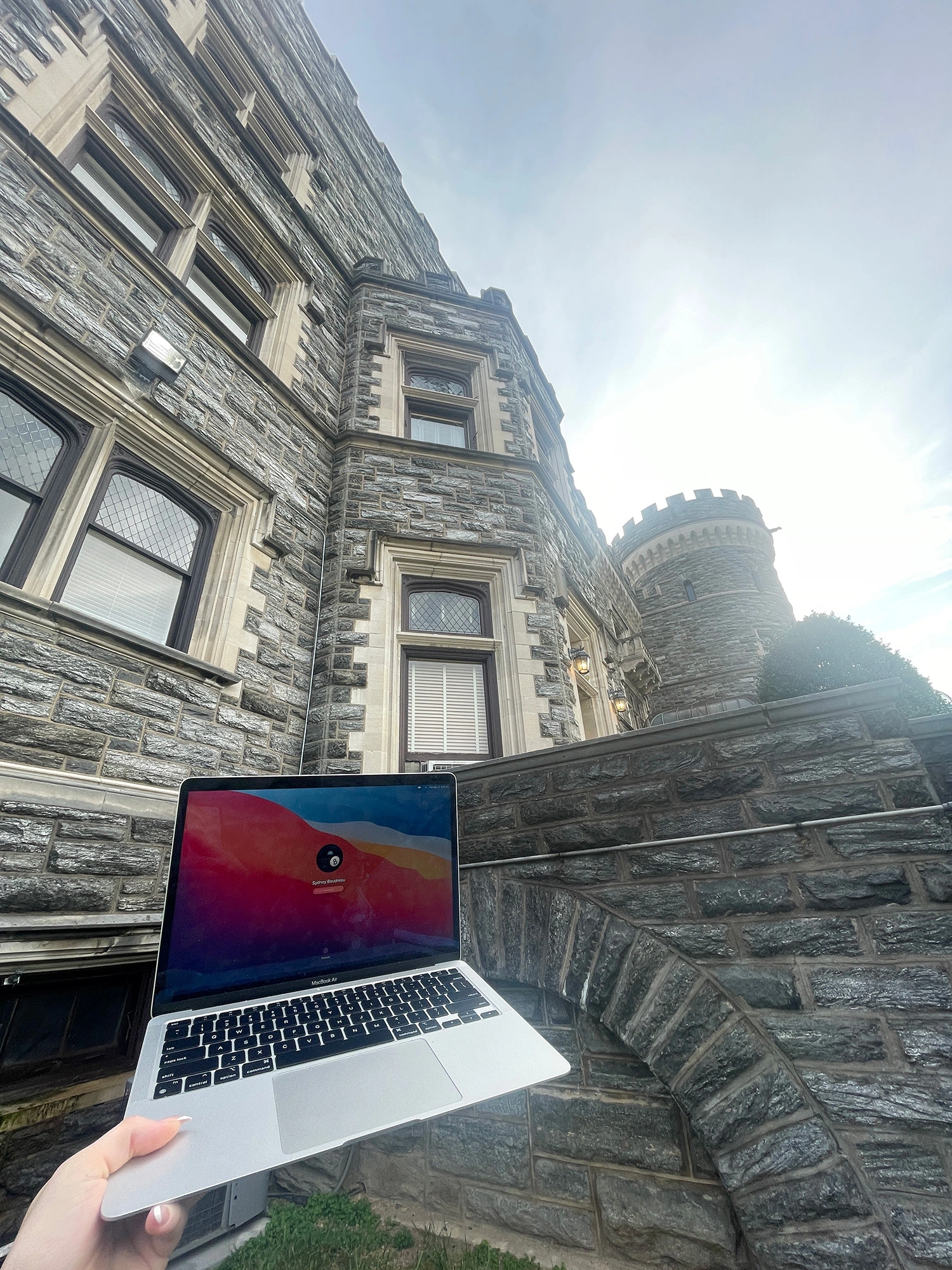 A laptop being held up next to Grey Towers Castle.