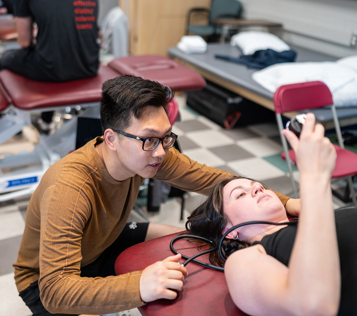 Two physician assistant students work in a practice clinical setting for PT and use a medical monitoring device.