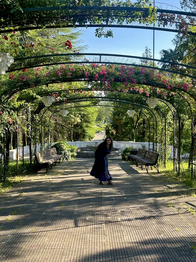 A woman wearing a dress poses beneath an archway of flowers