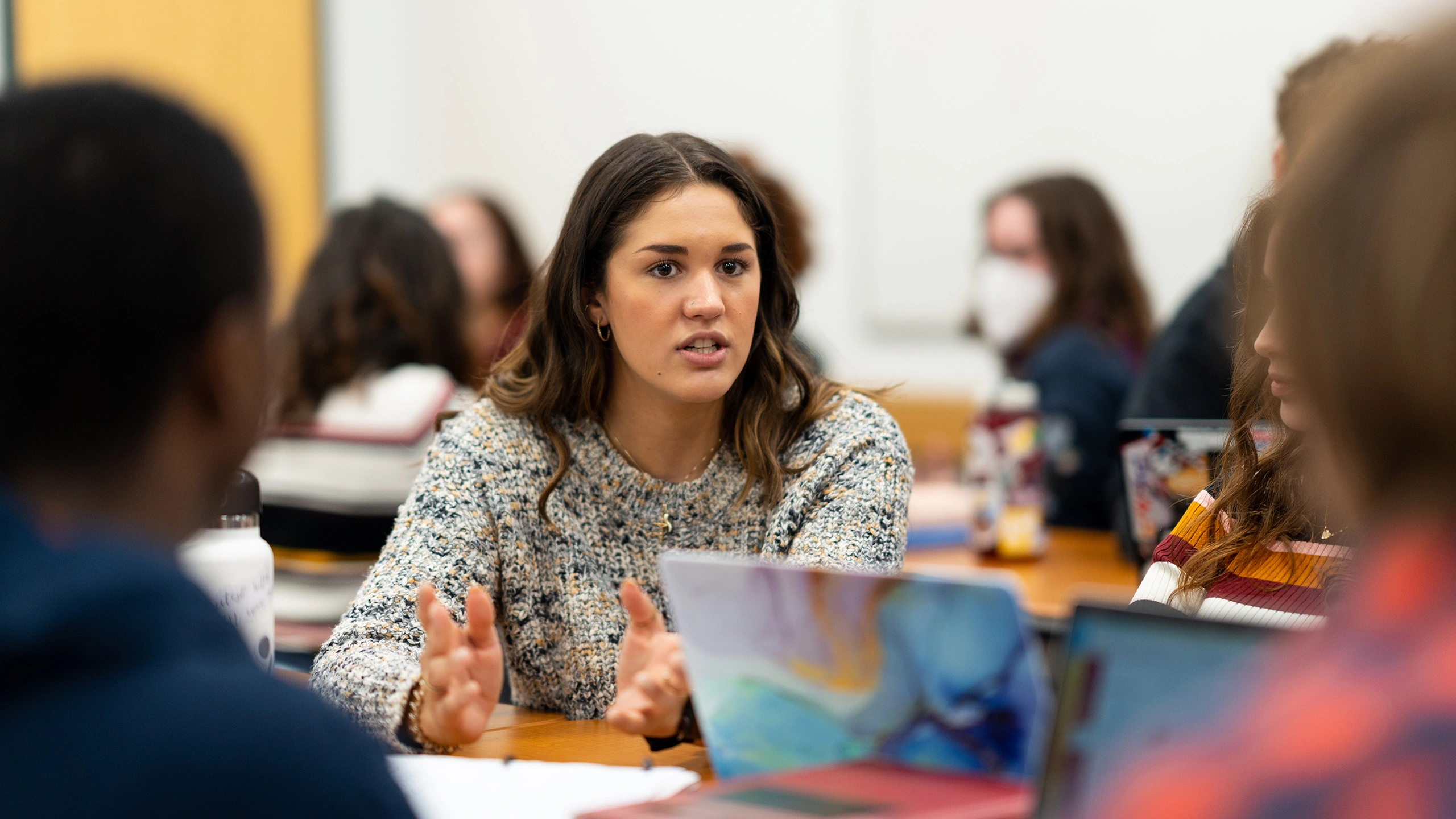 A student sits at long table and talks with her hands open during an undergraduate HAPS class.