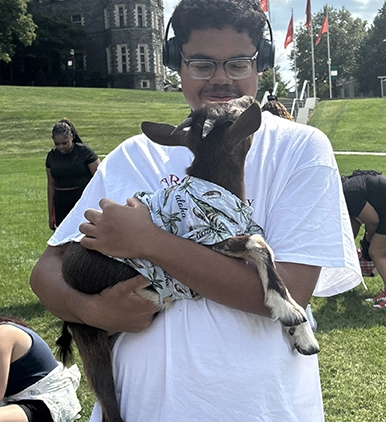 A particpant in the H.O.M.E. program holds a baby goat during an outdoor event on campus.