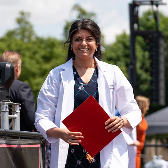 A physician assistant graduate holds her red diploma and stands proudly on the podium during commencement.