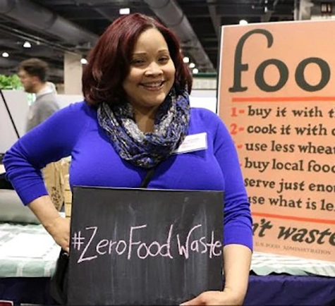 Alishah Powell, MSOD ’03, BAAU President stands by a zero food waste sign.