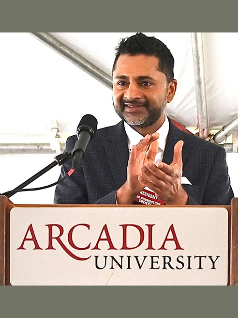 Presaident Nair stands at a podium and claps his hands furing an Alumni-sponsored Women Who Lead event.