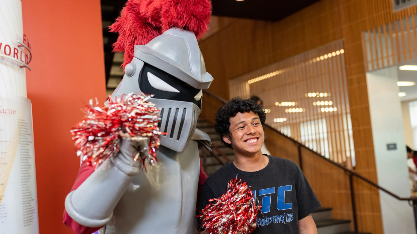 Archie give and an undergraduate student hold grey and red pompoms and give a cheer.