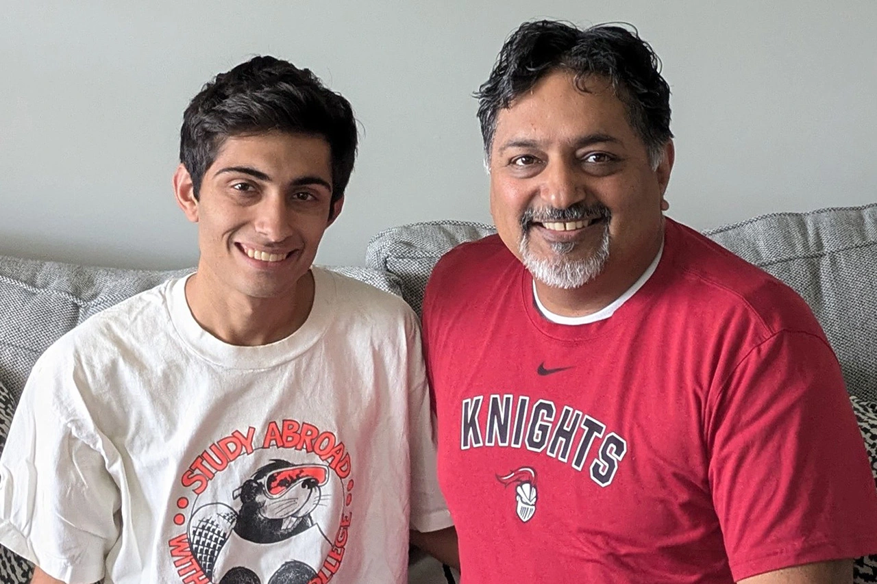 A father and his son both wear Arcadia t-shirts and sit on a gray couch.