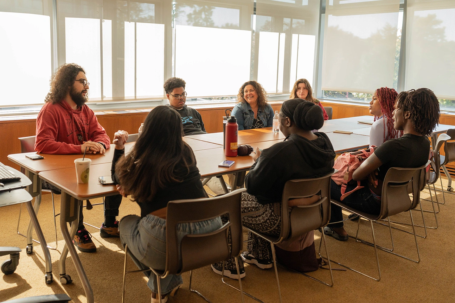 Resident life staff and students meet around a long sun-lit table in a conference room.