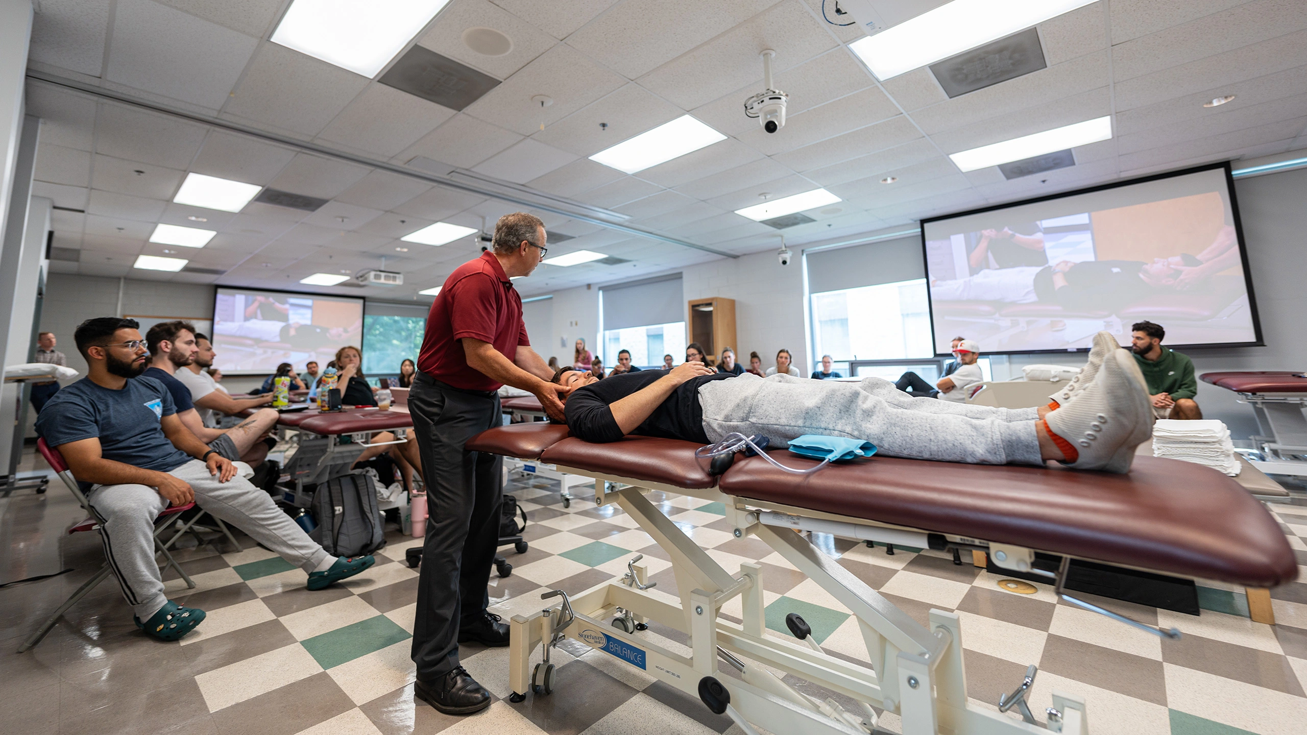 Physical therapy students watch a lab demonstration in a large room.