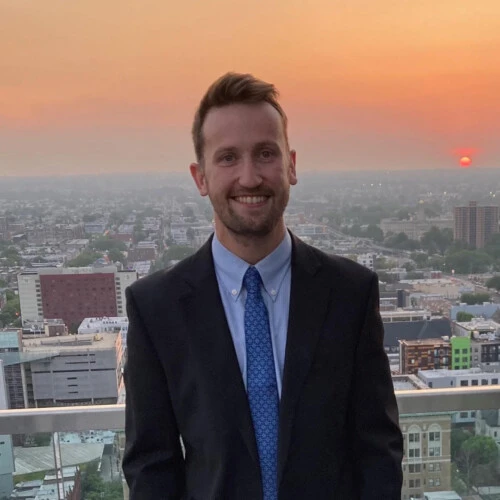 James Shaw profile image, man in suit with city at sunset behind