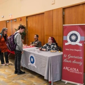 a student and staff member sit at a table next to a banner that reads "1st generation honor society"